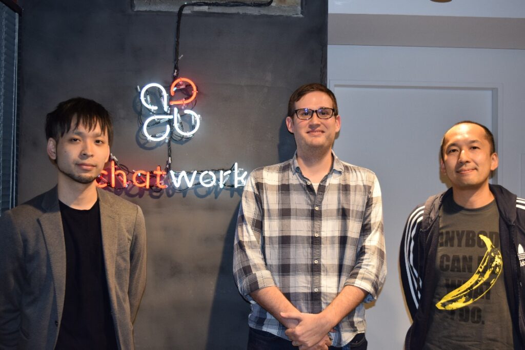 Three software engineers standing in front of a sign for a company called Chatwork.